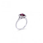 18ct white gold ring featuring a 1.06ct cushion-cut ruby in a four-claw setting with a cushion-shaped diamond halo and claw-set shoulders.