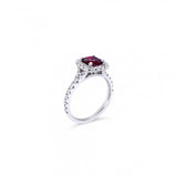 18ct white gold ring featuring a 1.06ct cushion-cut ruby in a four-claw setting with a cushion-shaped diamond halo and claw-set shoulders.