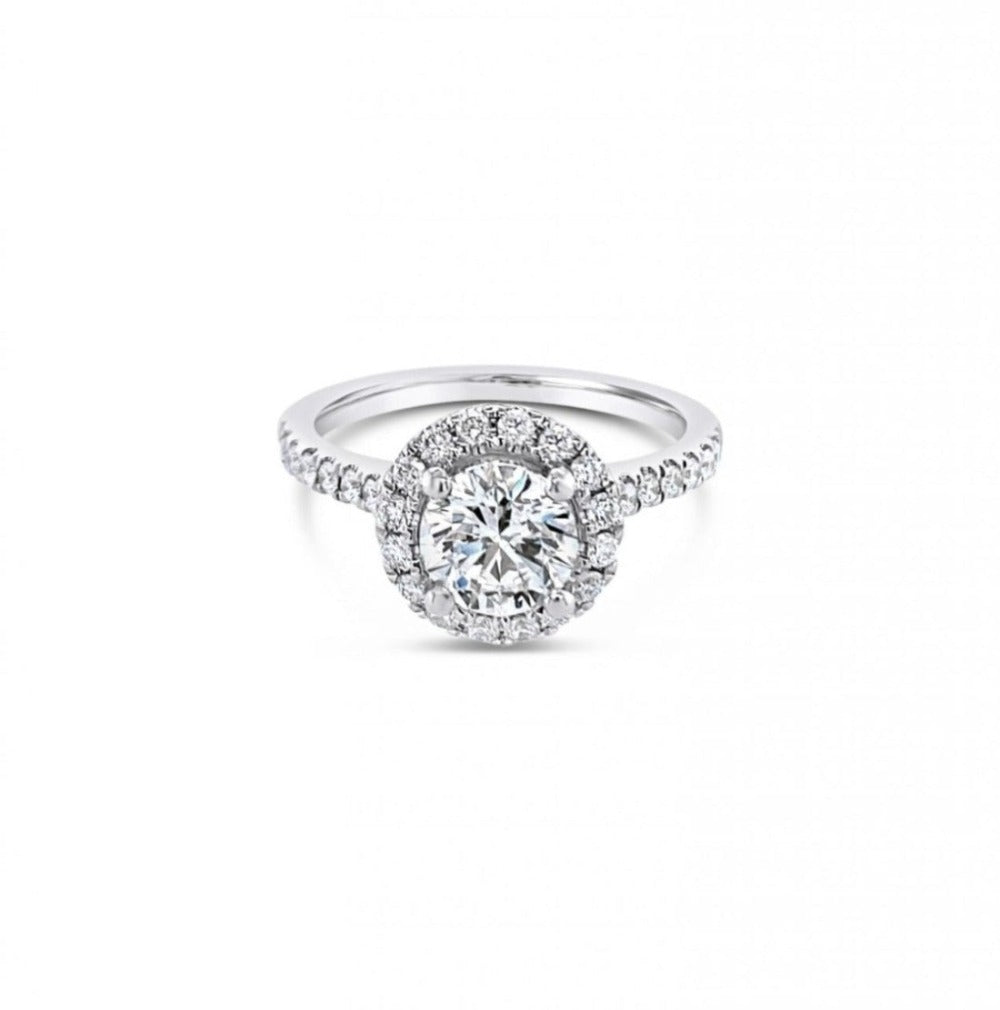 18ct white gold diamond halo ring featuring a 1.01ct round brilliant cut centre diamond with a circular diamond halo and claw-set shoulders.