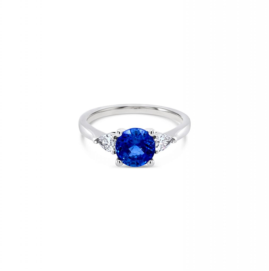 18ct white gold ring featuring a 1.32ct round-cut sapphire with pear-cut diamond accents totalling 0.25ct in elegant claw settings.